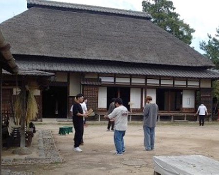 写真7、地域理解実習Ⅲ(富士見市内フィールドワーク、移築された古民家の前で、昔の遊具で遊ぶ体験)